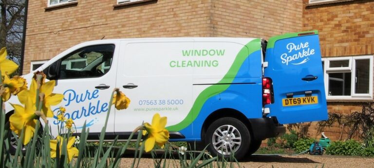 Window cleaning van with door open about to start cleaning windows. Setting is garden in spring in Surrey. Yellow flowers in front of van which is green and blue. Pure Sparkle is the brand on the van.